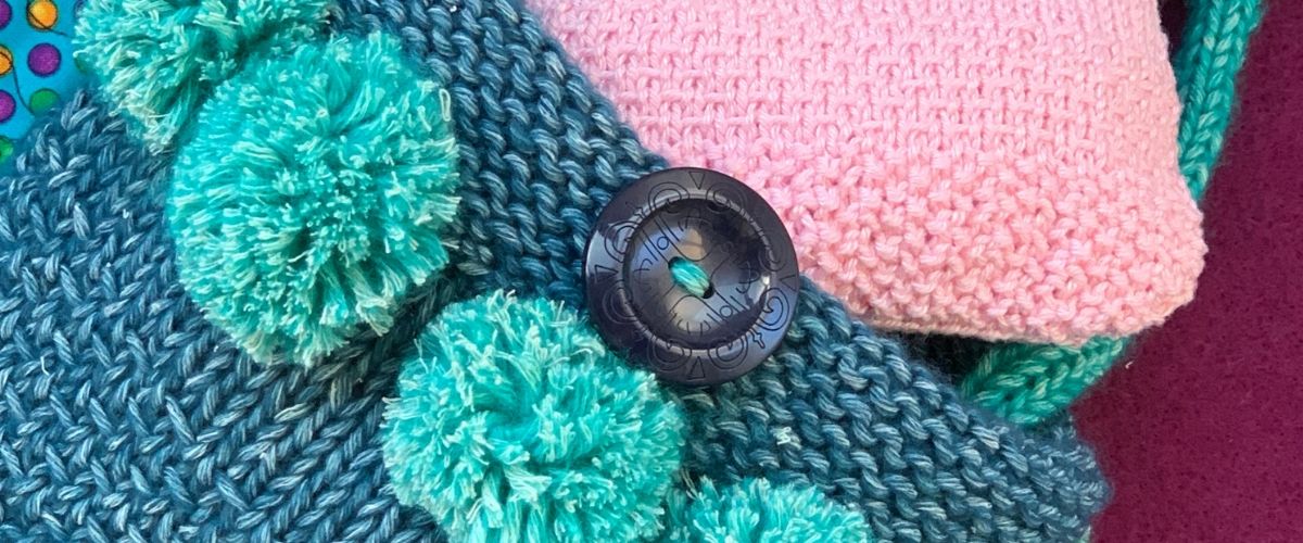 A hand knitted bag with pom-poms.