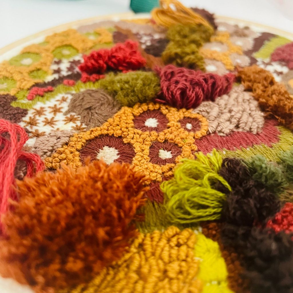 Close up of a detailled hand embroidery piece by Bethan Rhodes, featuring warm, autumnal tones