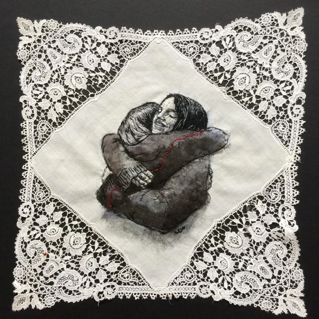 Mixed media and embroidery work of two women hugging stitched onto a hanky, by Lesley Wood